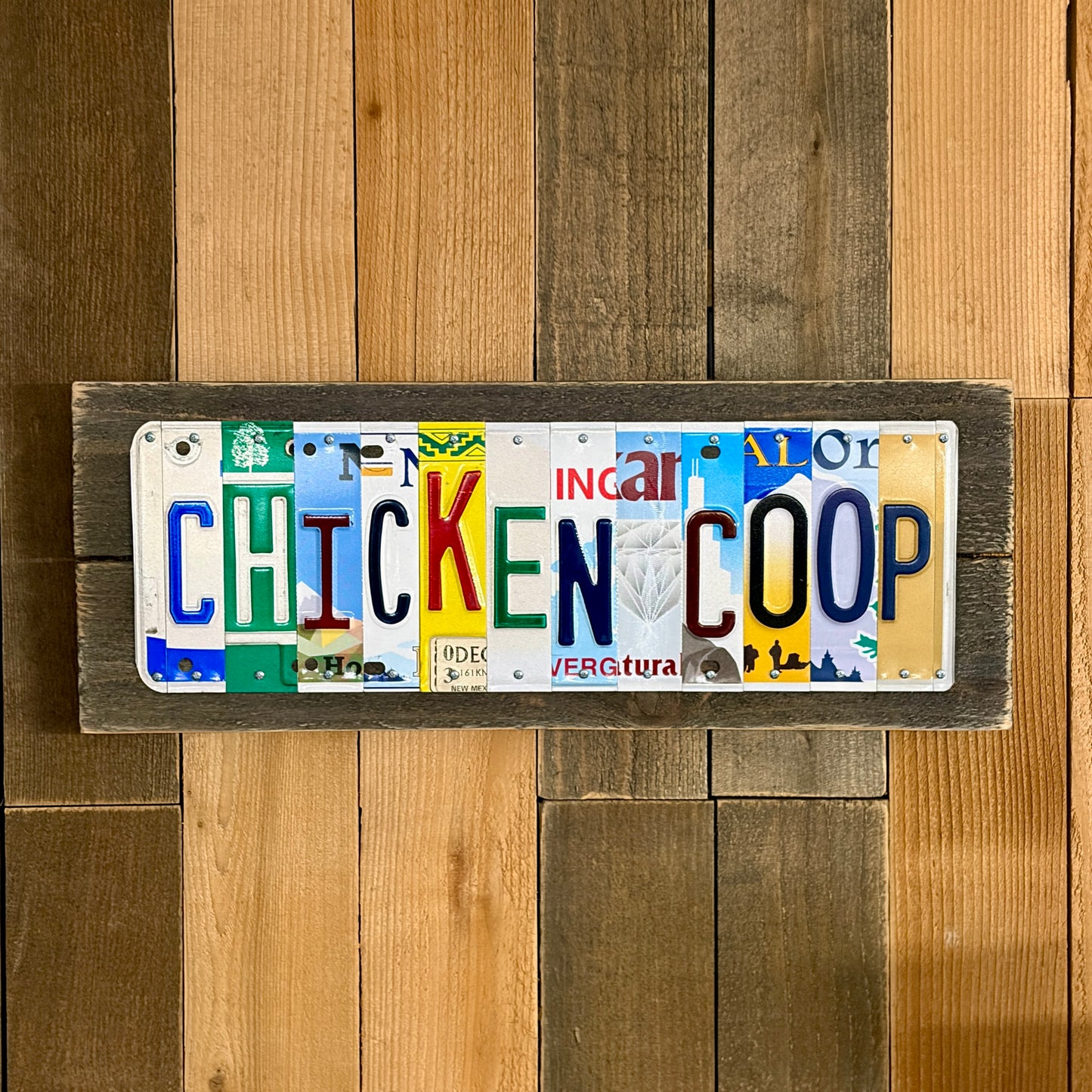 Decorative sign made from license plates with 'CHICKEN COOP' text on a wooden background