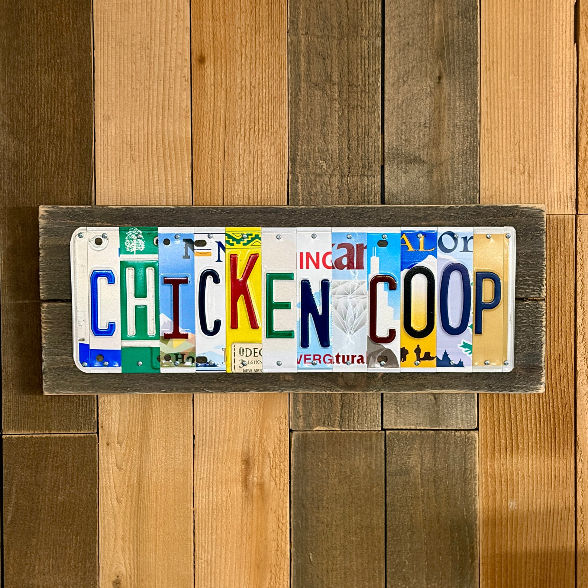 Decorative sign made from license plates with 'CHICKEN COOP' text on a wooden background